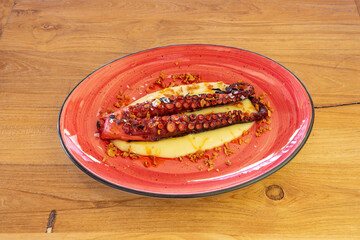 Two tentacles of grilled octopus on a bed of mashed potatoes in a nice red plate