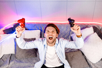 Euphoric winner guy raising up hands with wireless gamepad controllers, celebrating victory online...