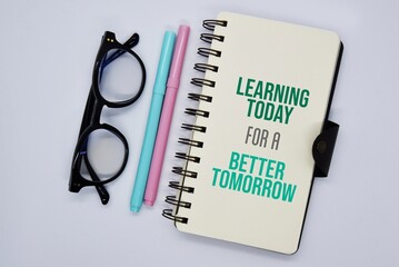 'Learning today for a better tomorrow' quote on the notebook with two pen and spectacles white...