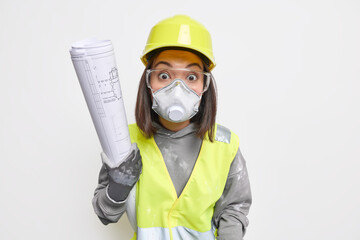 Surprised young Asian female builder or engineer develops new plan wears protective helmet and mask transparent glasses develops new building plan holds blueprint isolated over white background