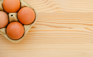 Fresh chicken brown eggs in a cardboard egg box on a wooden background. Top view.