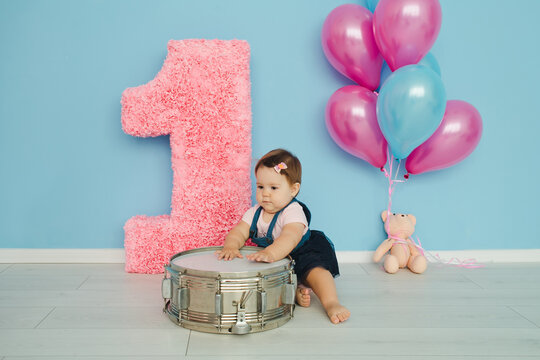 Little cute girl celebrates her birthday at 1 year old. The little girl smiles and crawls against the background of number one, fairy balls, drum and a blue wall