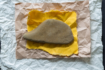 crumpled paper background - layered yoke yellow, beige, and off white winkled and flattened sheets of various sizes and a grey brown sand stone on a dark ground 