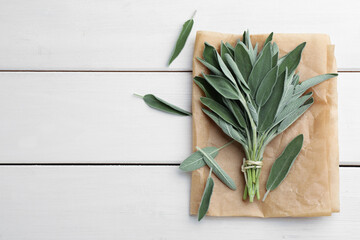 Bunch of fresh green sage with parchment on white wooden table, flat lay. Space for text