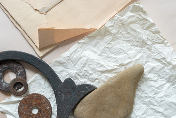 Fototapeta na wymiar flat, folded, and crumpled paper with vintage ironwork object, rusty washers, and sand stone - photographed from above in a flat lay style