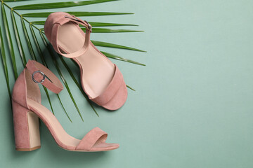 Pair of stylish high heeled shoes and palm branch on green background, flat lay. Space for text