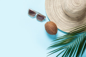 Women's hat with wide brim, sunglasses, coconut and a branch of a palm tree on a blue background. Summer concept, vacation at sea. Banner. Flat lay, top view