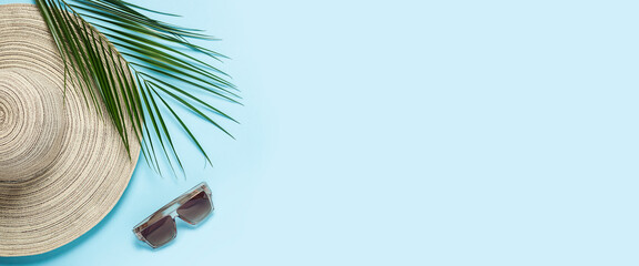 Women's hat with wide brim, sunglasses and a branch of a palm tree on a blue background. Summer concept, vacation at sea. Banner. Flat lay, top view