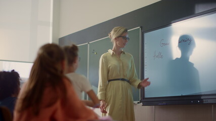 Young schoolteacher and schoolgirl standing at smart board in classroom