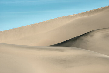 The smooth lines of sand dunes under the blue sky. Close-up.