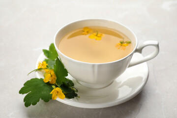 Cup of aromatic celandine tea and flowers on grey table, closeup