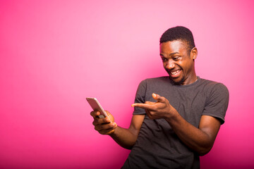 Happy as a winner excited young black Man using smart phone isolated over pink background. Emotional young caucasian guy won the lottery big sum of money, huge success 