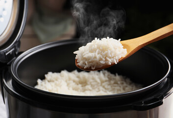Spoon with tasty hot rice over cooker, closeup