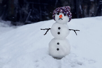 Sad snowman in hat on snowy background