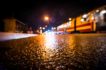 Fototapeta premium Night city after rain, the cars and tram driving on the road. View from a wide angle at the level of the asphalt