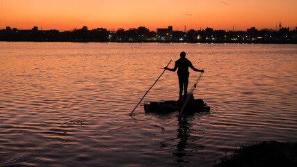 Fisherman on a small boat catching freshwater fish in nature river during sunset