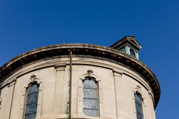 Fototapeta na wymiar Exterior of a stone church building with stained glass windows, verdigris copper details against a deep blue sky, horizontal aspect