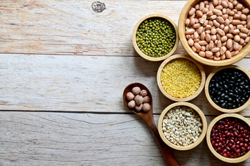 Dried peanuts, Hulled-split Mung Bean (Yellow beans), Mung Beans, Red beans, Black Beans, Millet grains are in the wooden bowl and Lotus seed in Wooden Spoon on the wooden table.