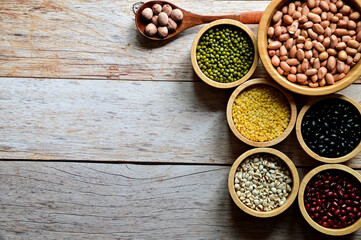 Dried peanuts, Hulled-split Mung Bean (Yellow beans), Mung Beans, Red beans, Black Beans, Millet grains are in the wooden bowl and Lotus seed in Wooden Spoon on the wooden table.