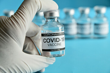 Doctor or nurse holding Coronavirus COVID-19 Vaccine Glass Bottle on blue surface with blue background at Thailand. Concept viruses spread throughout the world. Selective Focus.