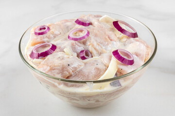Raw chicken meat marinated with mayonnaise or sour cream sauce, pepper, onion in a bowl on white background
