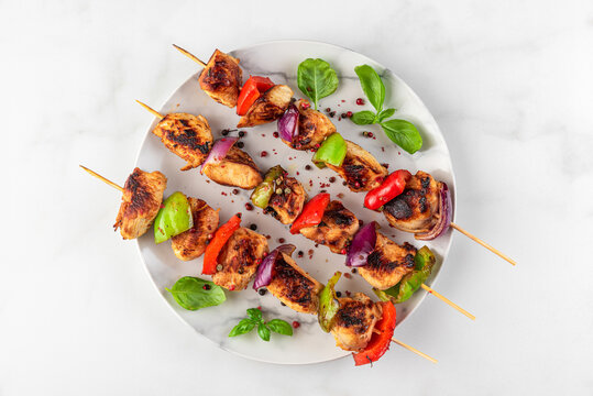 Chicken breast fillet grilled barbecue skewers with vegetables and basil in a plate on white table. top view