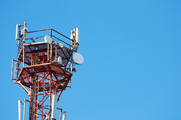 A telephone metal tower of red and white radio communication hung with equipment and satellite dishes against the blue sky. Modern technology and communication communications. Copy space.