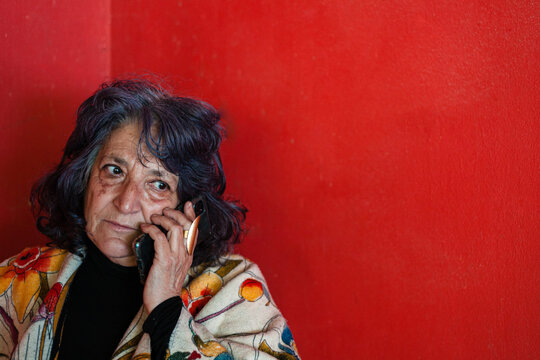 Closeup Shot Of An Elder Hispanic Female Talking On The Phone Near A Red Wall