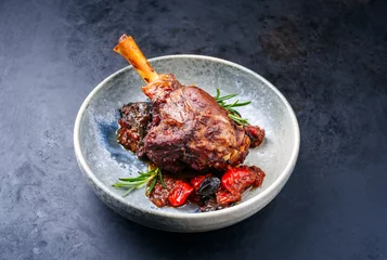 Poster Modern style traditional braised slow cooked lamb shank in red wine sauce with eggplants and tomatoes served as close-up in a design bowl © HLPhoto