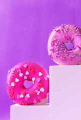 Pink donuts with different icings on white podiums against the purple background