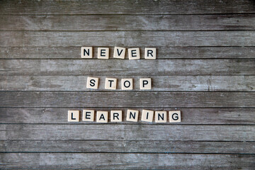 never stop learning phrase made from plastic letters on rustic wooden background. Horizontal, copy space, flat lay top view