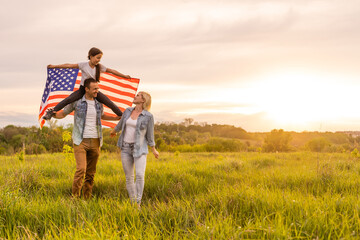 Beautiful family with the American flag in a field at sunset. Independence Day, 4th of July.