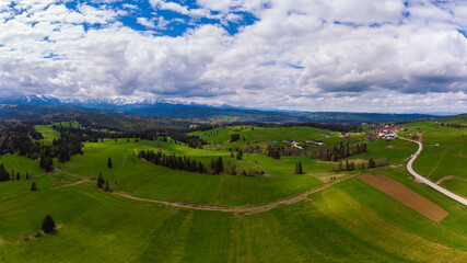 View from above on beautiful green meadows, snow-capped peaks of the Tatra Mountains in the distance. View from the air. View from the drone.