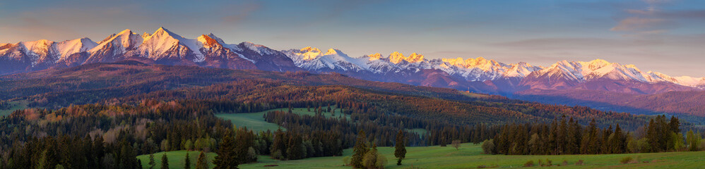 A beautiful panorama of the entire range of the Tatra Mountains. The colorful rays of the sun illuminate the snow-covered, white mountains. The view at sunrise. Poland