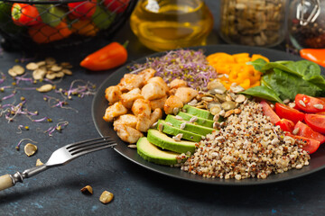 Salad with quinoa, avocado and chicken. Front view. Served on a black plate.
