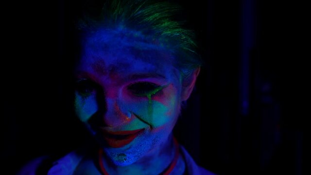 horror makeup in UV light, female face with fluorescent paints in flashes of light in darkness