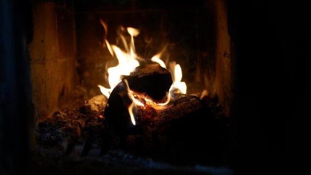 4K video, static camera clip of a fireplace with a flame burning a bright flame of firewood in the stove close-up. Red fiery coals warm the atmosphere of a home.