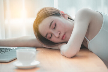 A woman wearing a white shirt slept in a white office with a coffee cup and a notebook on the table.