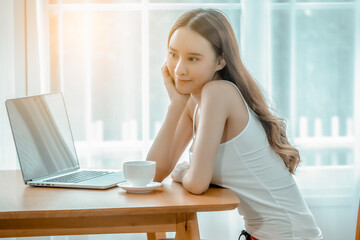 A woman in a white blouse sits in the office on the table with a white coffee mug and a notbook.