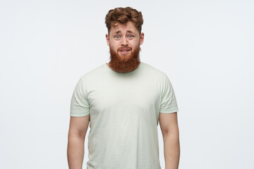 Fototapeta premium indoor shot of confused irritated young bearded male with red hair, wears blank t-shirt. isolated over white background