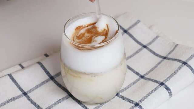 Woman person hand stirring latte coffee with caramel with glass spoon on a white table