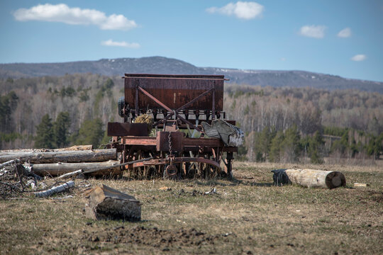 Old abandoned agricultural tractor on the farm. Beautiful mountains in the background. Blue sky. Abandoned agricultural machinery.