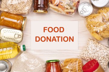 Food donations such as pasta, rice, oil, peanut butter, canned food, jam and other on white wooden table, top view with copy space