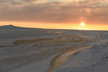 Arctic landscape in winter time. Small river with ice in tundra. Sunset.