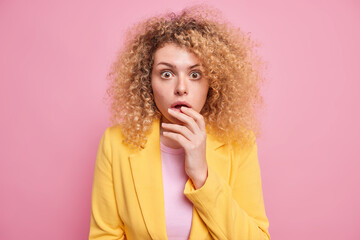 Portrait of surprised young woman with curly bushy hair stands ambushed stares speechless with...