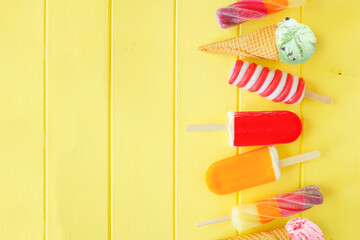 Variety of colorful summer popsicles and ice cream desserts. Top down view side border on a bright yellow wood background. Copy space.