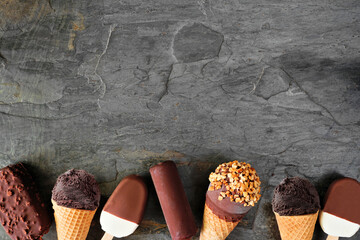 Assortment of chocolate ice cream desserts. Top view bottom border over a dark slate background...