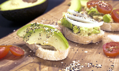Fresh vegan homemade sandwich with avocado, tomatoes, seeds on wooden cutting board, dark background. Top view of avocado sandwiches. Food photo, healthy food.