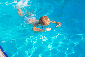 Cute happy little boy in goggles swimming and snorking in the swimming pool