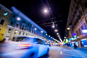 Nights lights of the big city, night avenue in the light of lanterns and passing car. Wide-angle view, defocused image